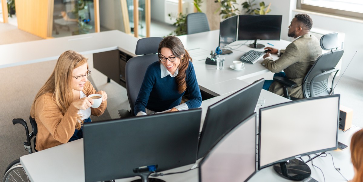 two women at a desk with large computer screen