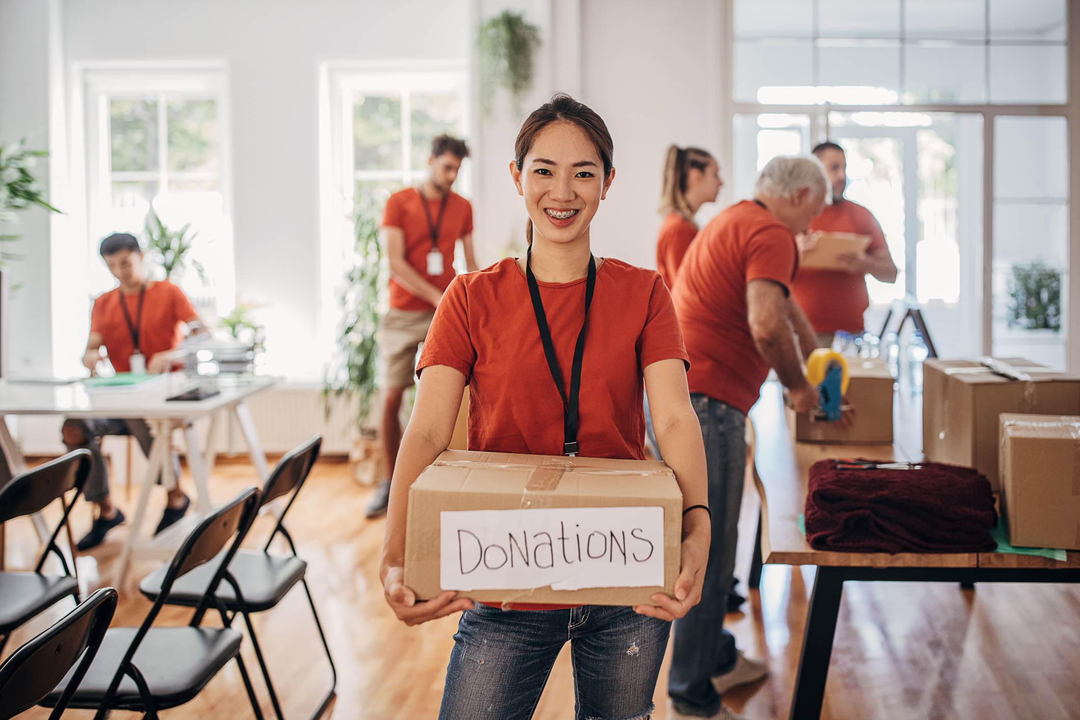 woman holding box labeled "donations" with several people working in background