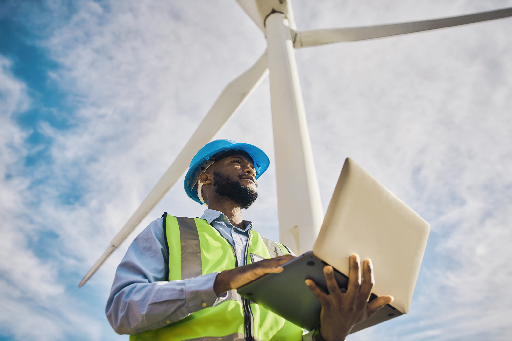 Man at a windmill energy plant using a tablet and looking out