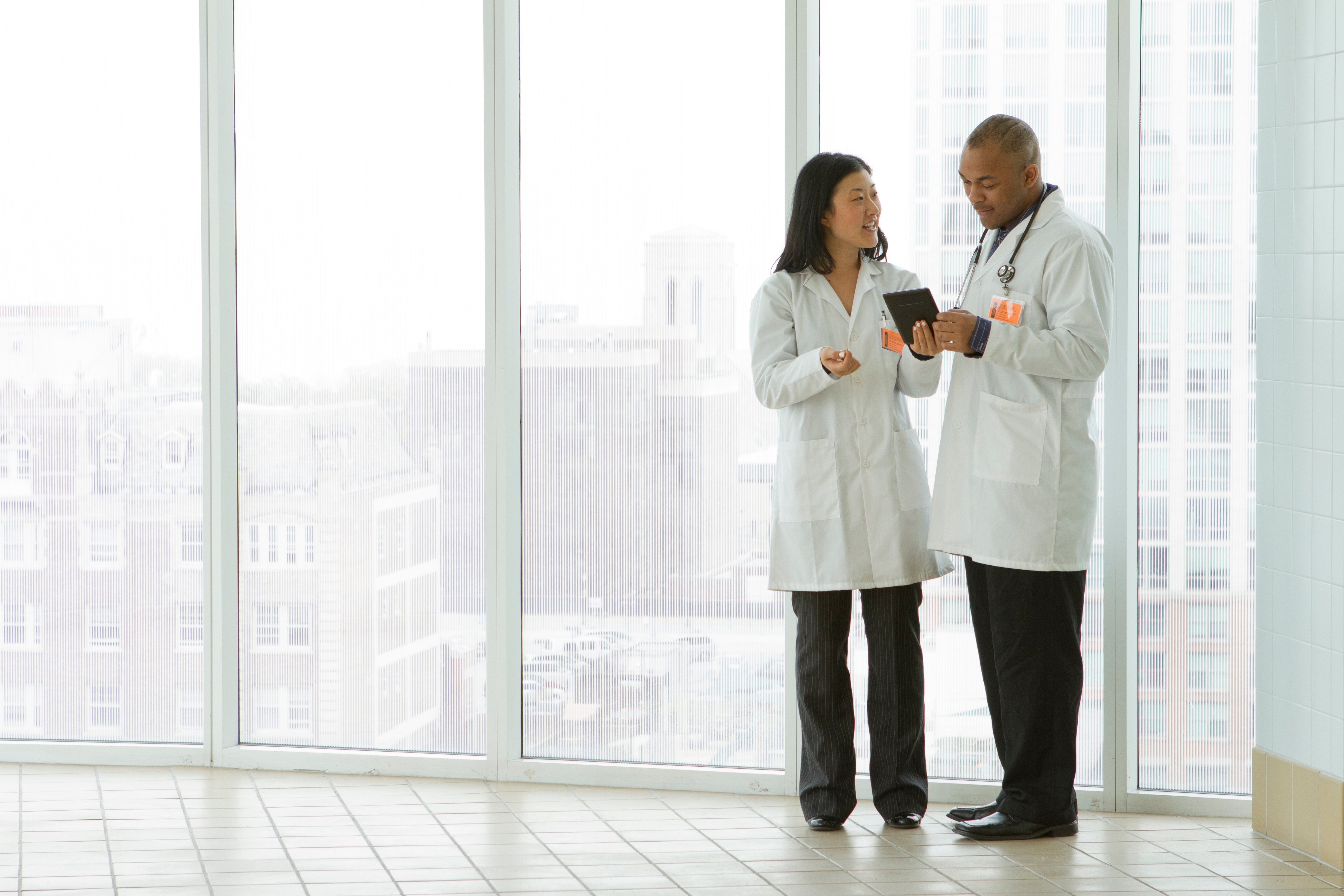 Two doctors standing in a hallway chatting looking at a tablet
