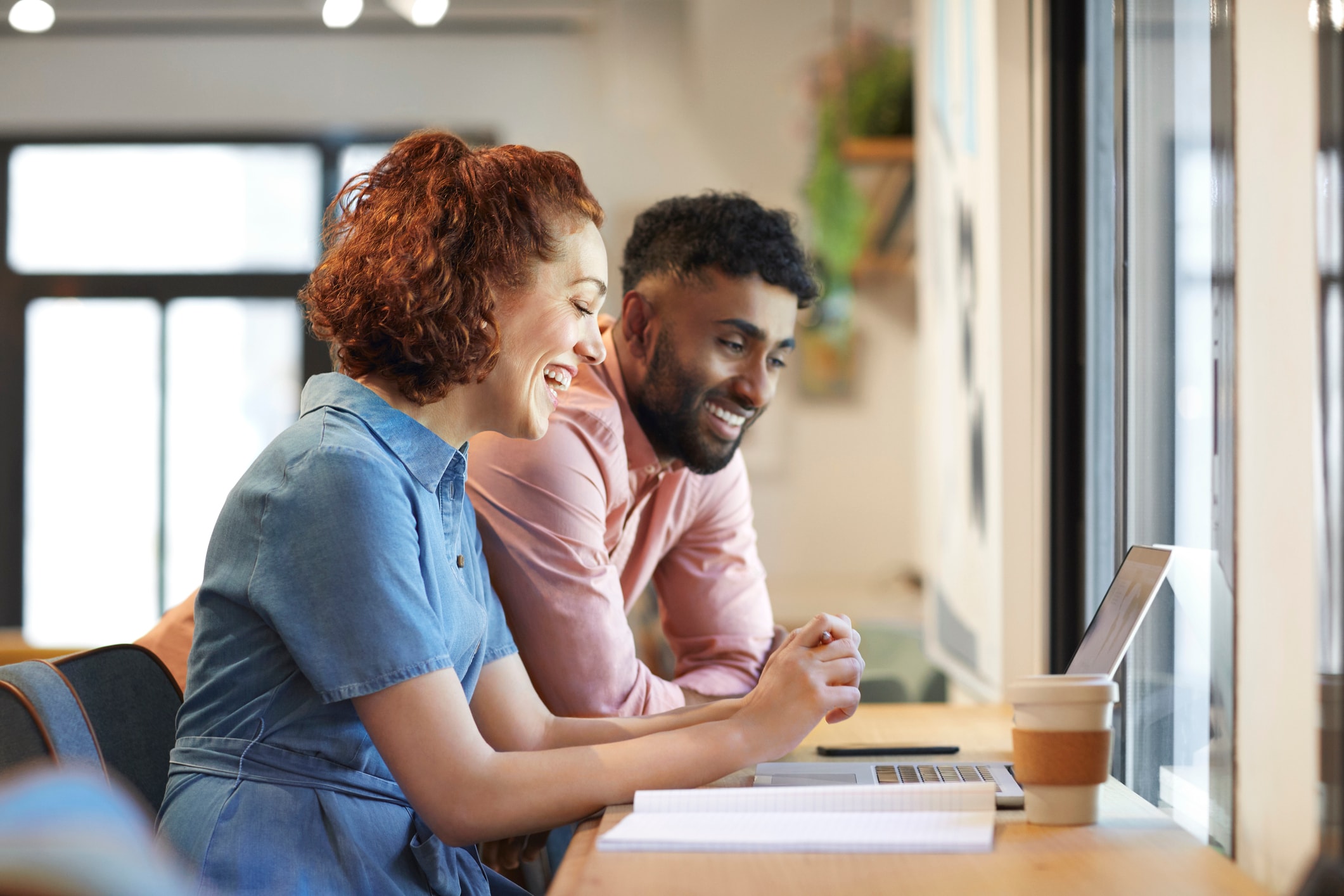 man standing, woman sitting, smiling at laptop
