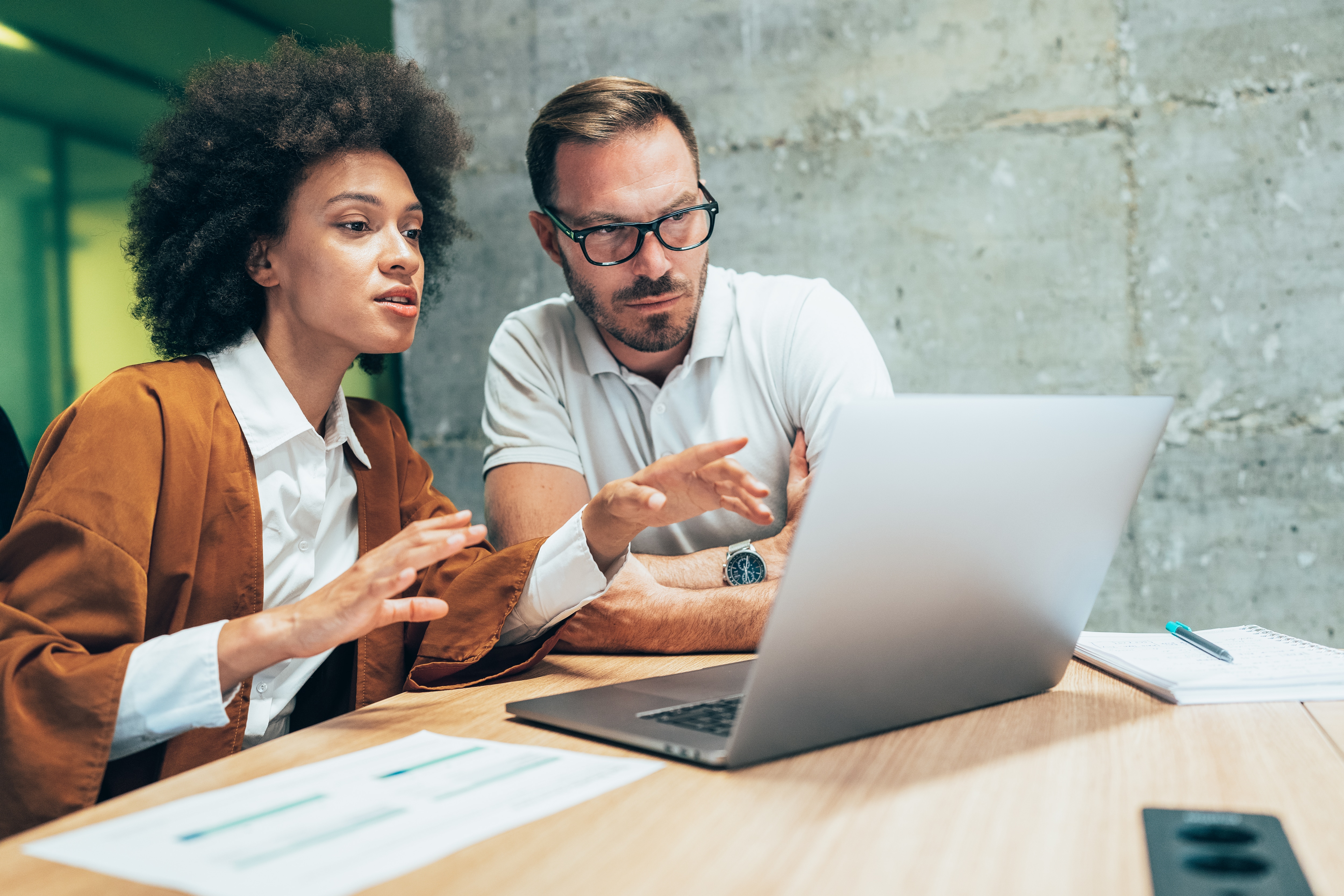 a man and woman look at the laptop screen