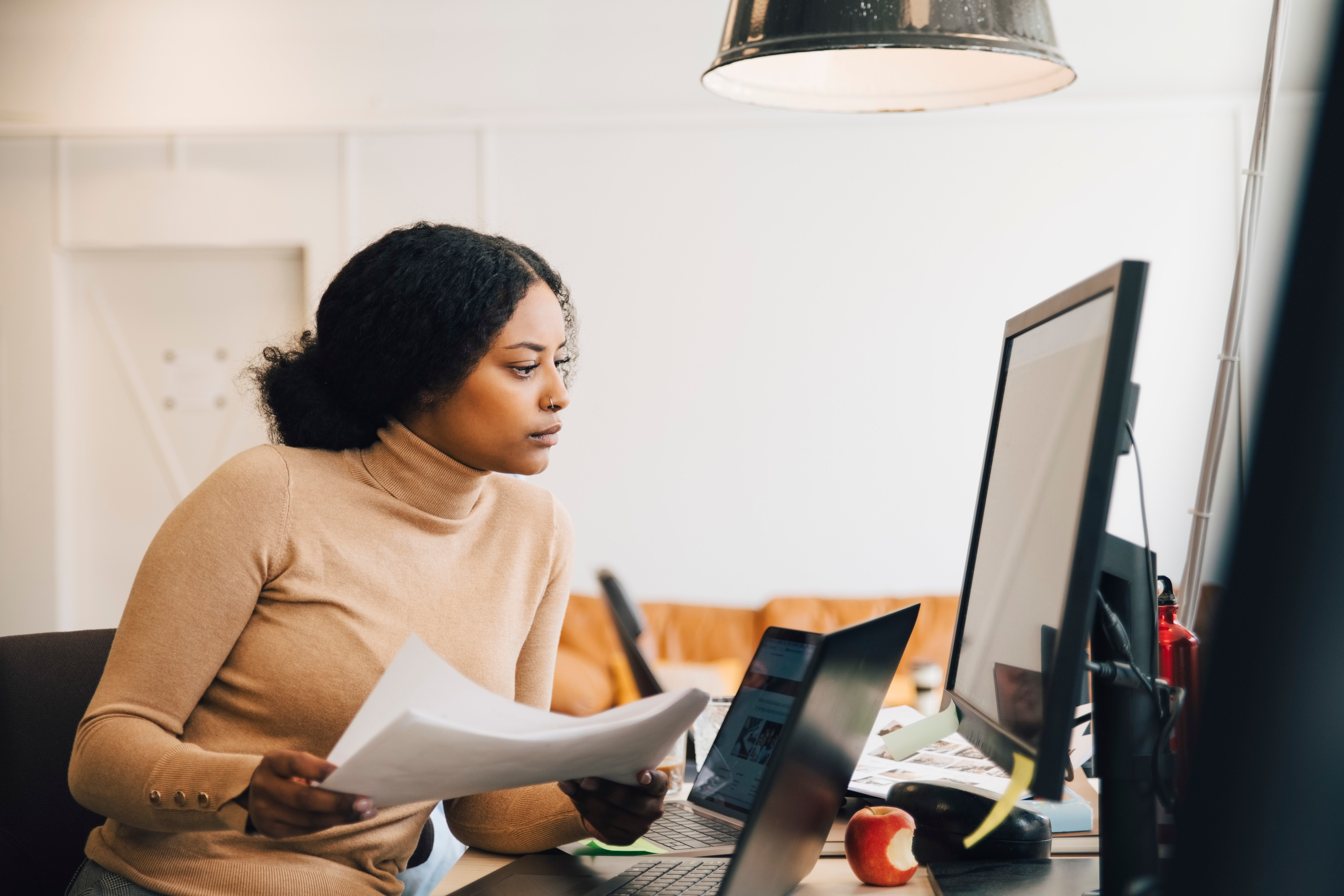 Woman with papers in her hand looking at a computer