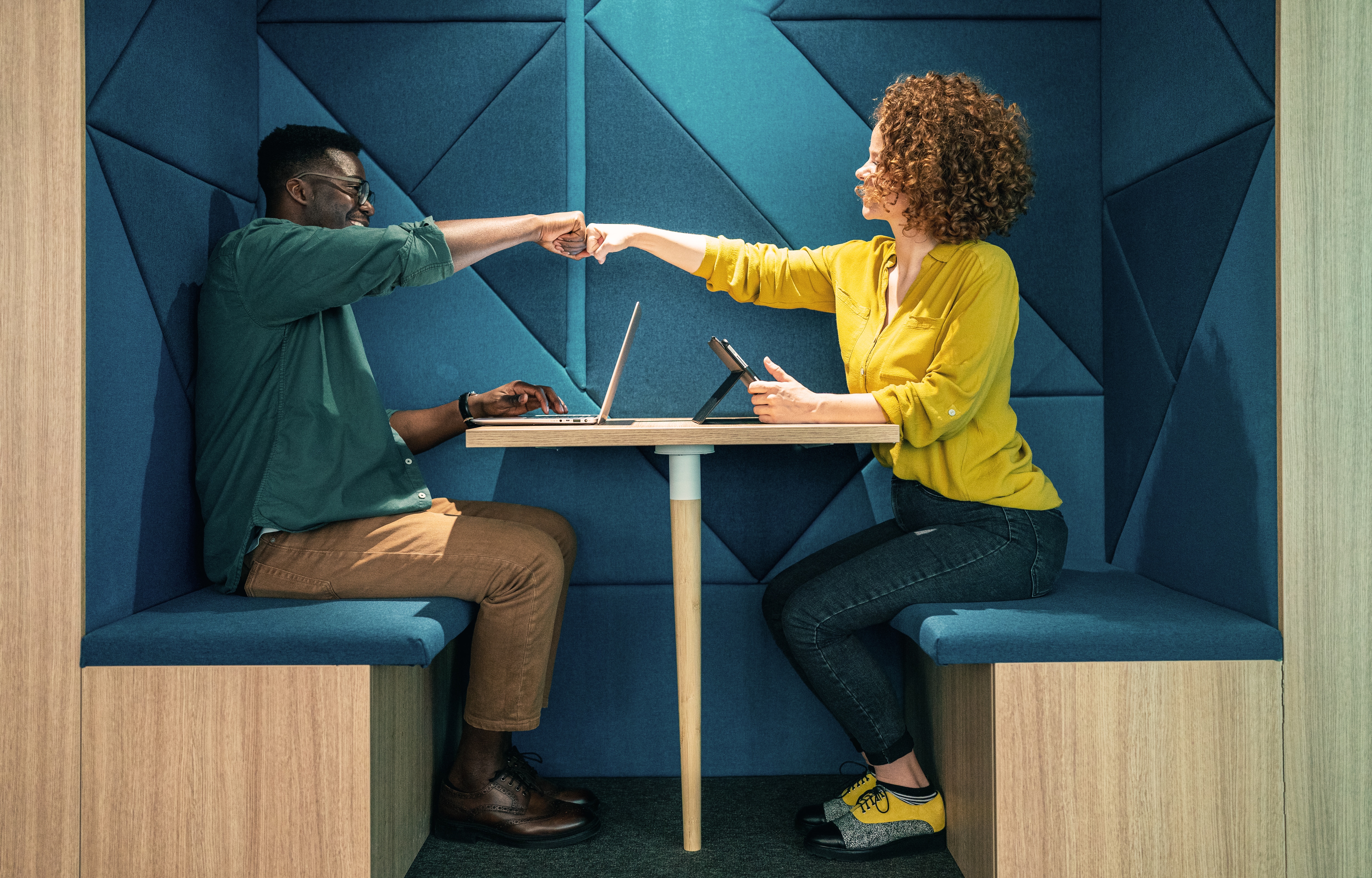 Two people in office fist bumping each other