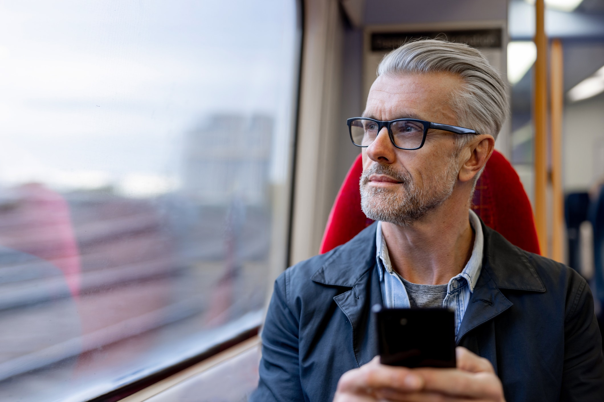 Man looking out window in moving train holding cell phone
