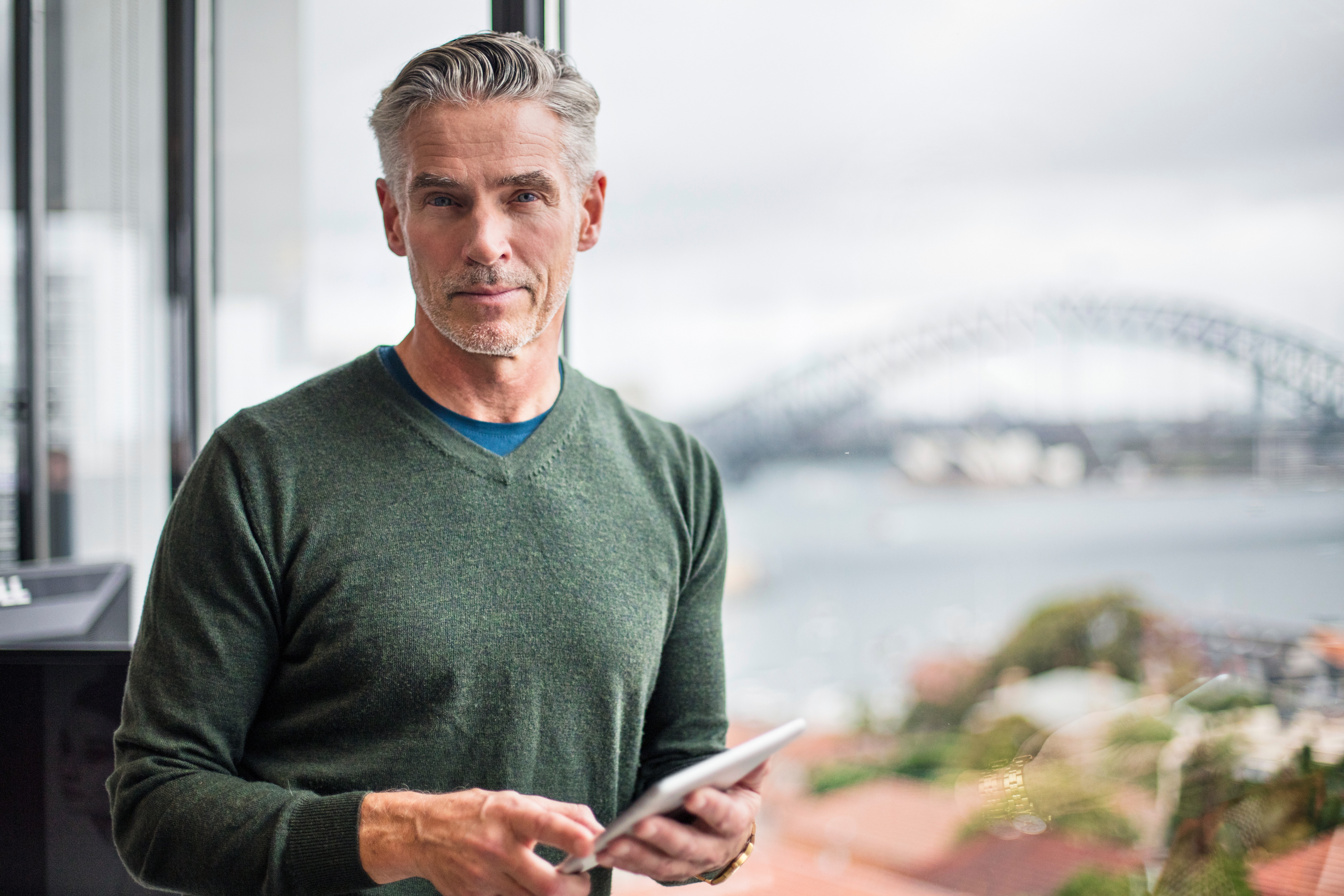 man standing at window holding tablet