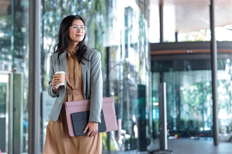 Lady holding coffee and walking with lap top thinking about submitting her expenses