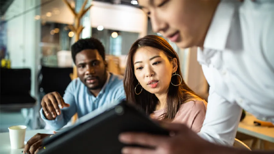 three people working in an office looking at a tablet
