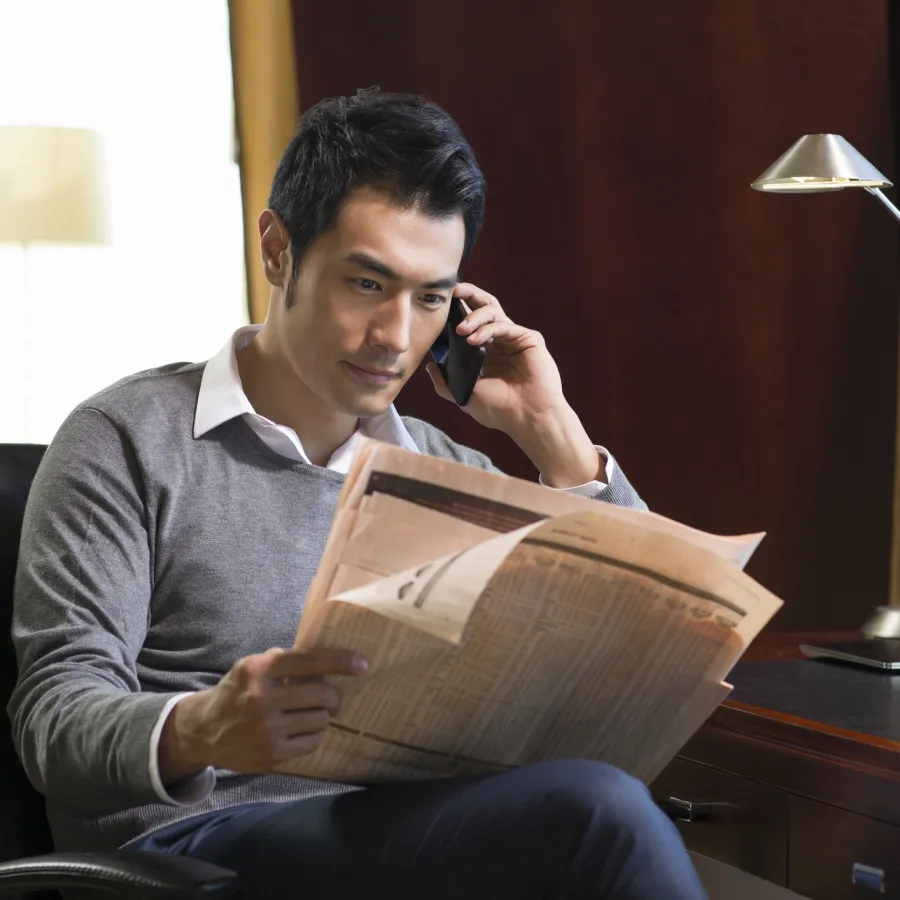  Young businessman reading newspaper and talking on phone