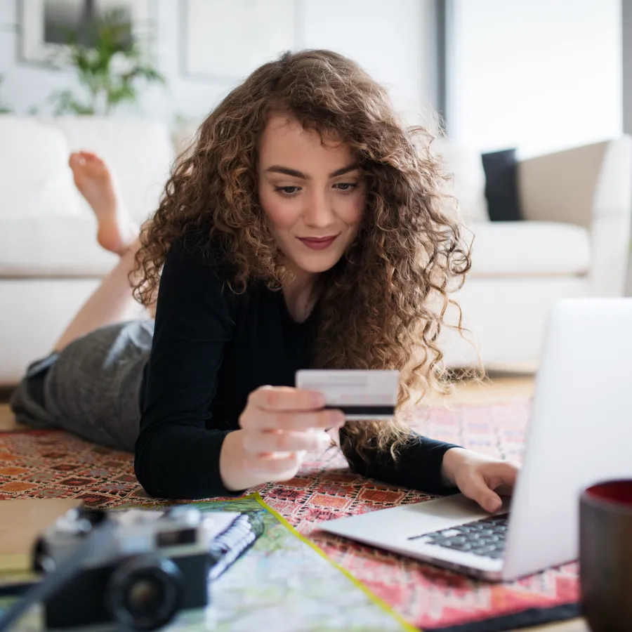 A young woman with laptop, camera and map holding a card, making online payment