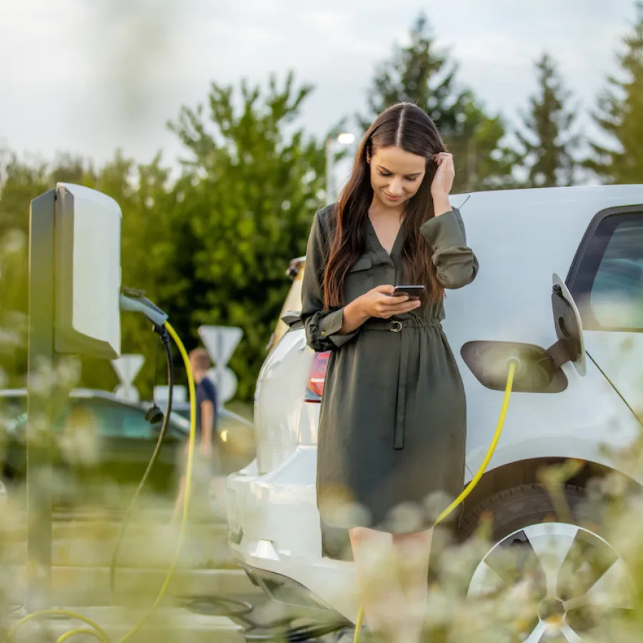 Woman using mobile phone while waiting for electric car to charge