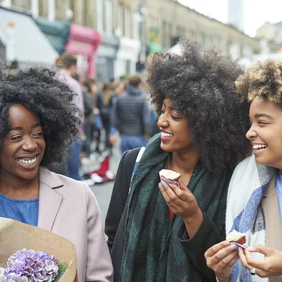 Three happy women walk down the street and eat pastries