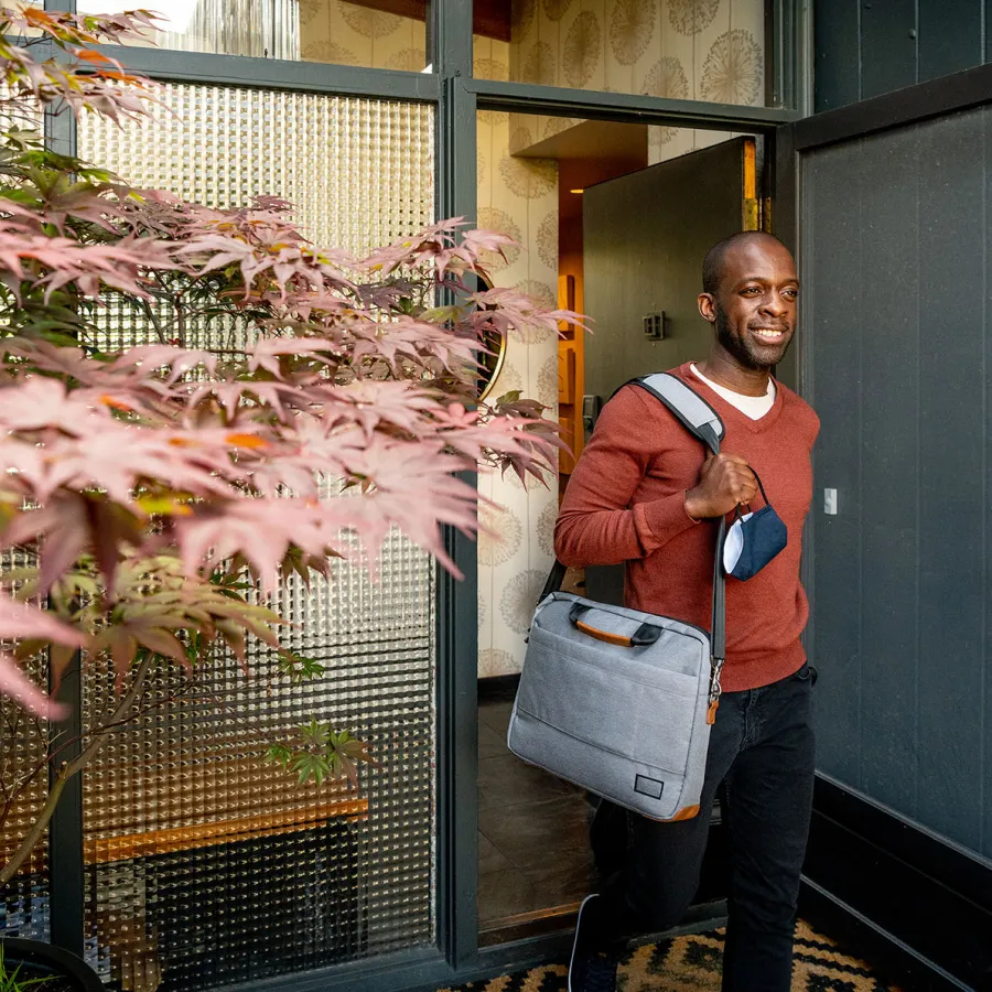 Business traveler leaves his house with a suitcase and tote bag