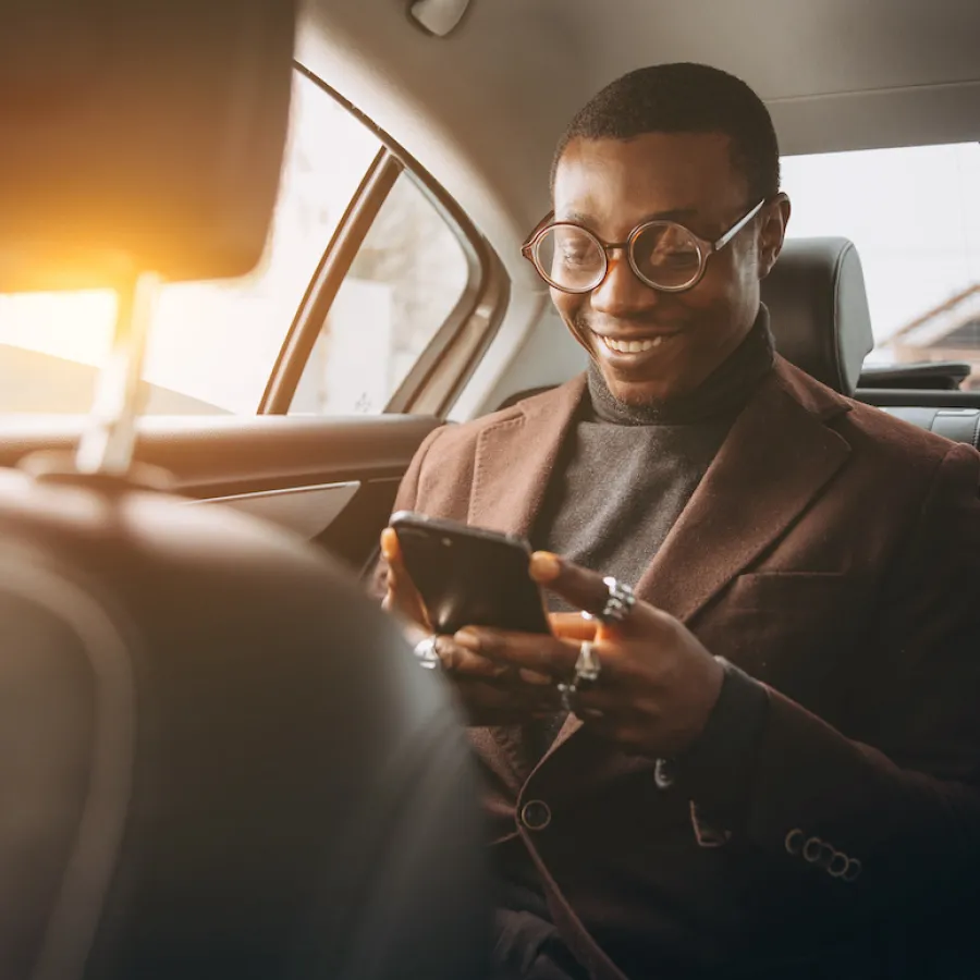 Young smiling man using smartphone while sitting on backseat in car.