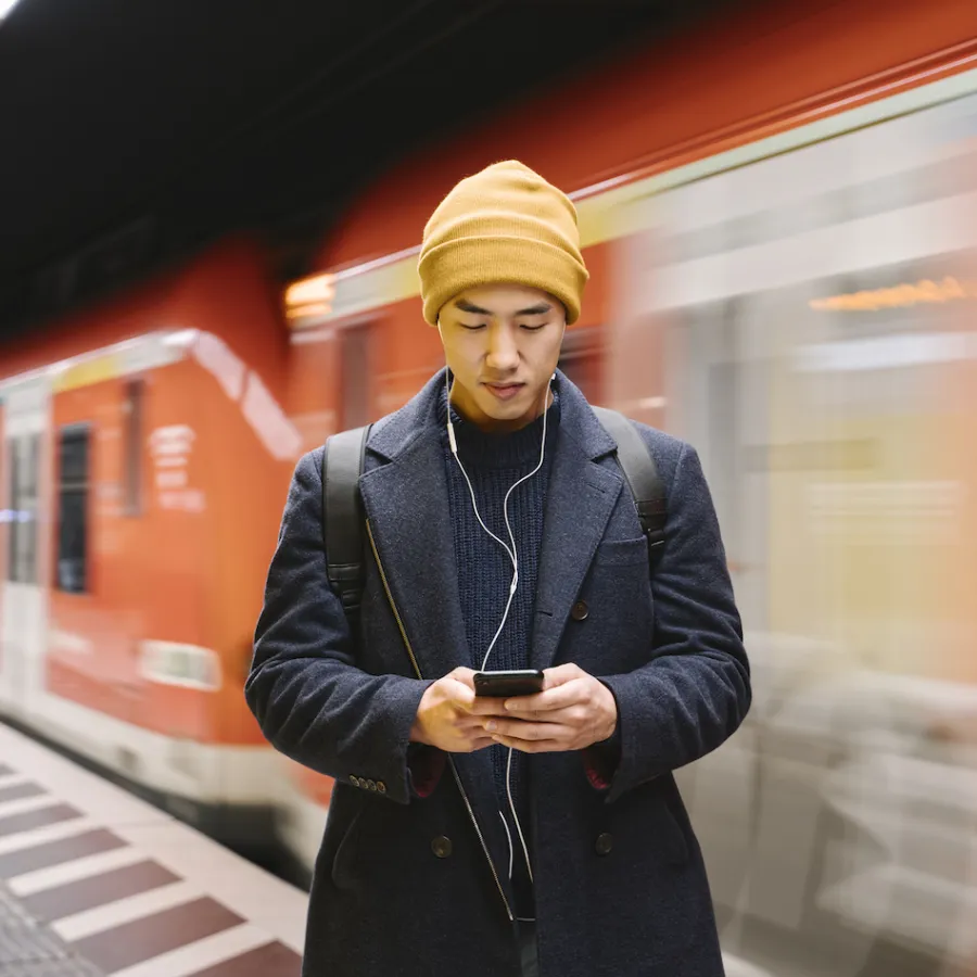 Stylish man with smartphone and earphones in metro station - stock photo