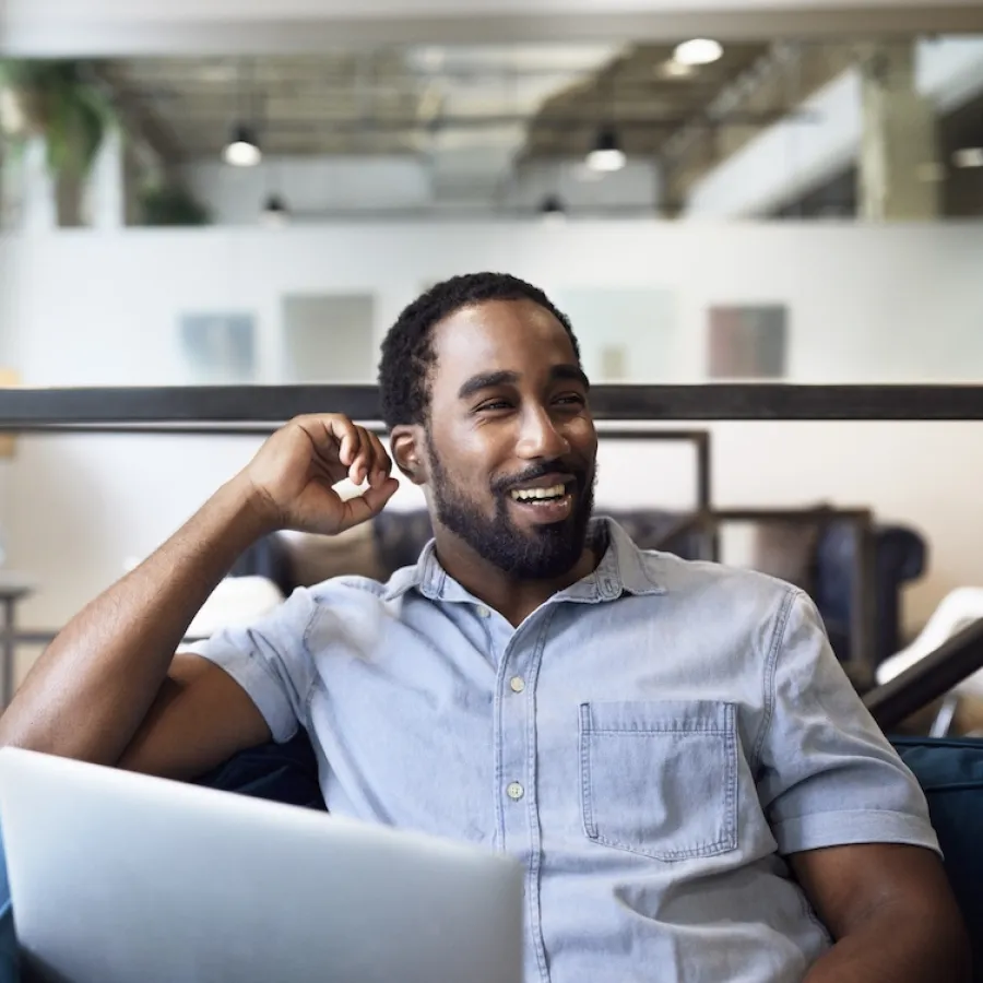  Happy businessman with laptop looking away while sitting on sofa at office - stock photo