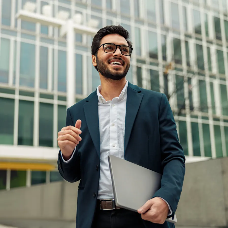 Man standing outside of office building holding closed laptop