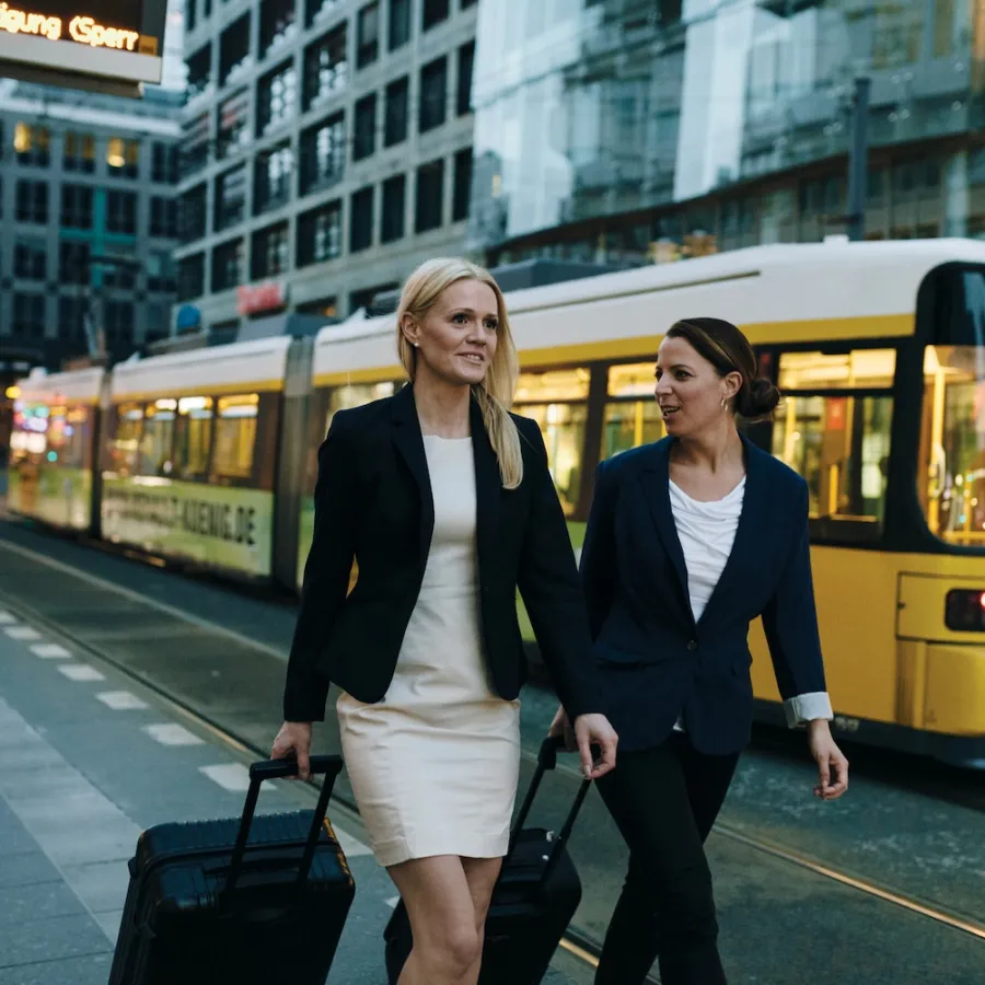 Two business women dressed in suites walking down the street with yellow bus in background